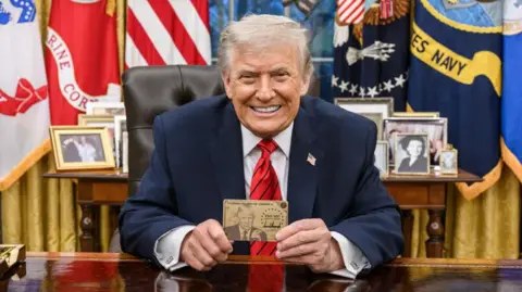 President Trump in the Oval Office holding up a 'gold card' visa